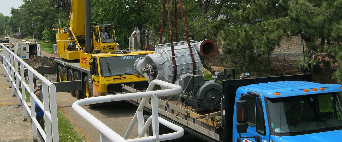 Large apparatus being transported off a flatbed trailer by a crane to be worked on